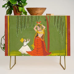A female attendant is standing in tribhanga pose under a tree. A small child vies for her attention. Credenza