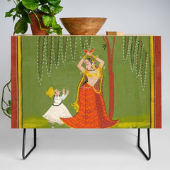 A female attendant is standing in tribhanga pose under a tree. A small child vies for her attention. Credenza